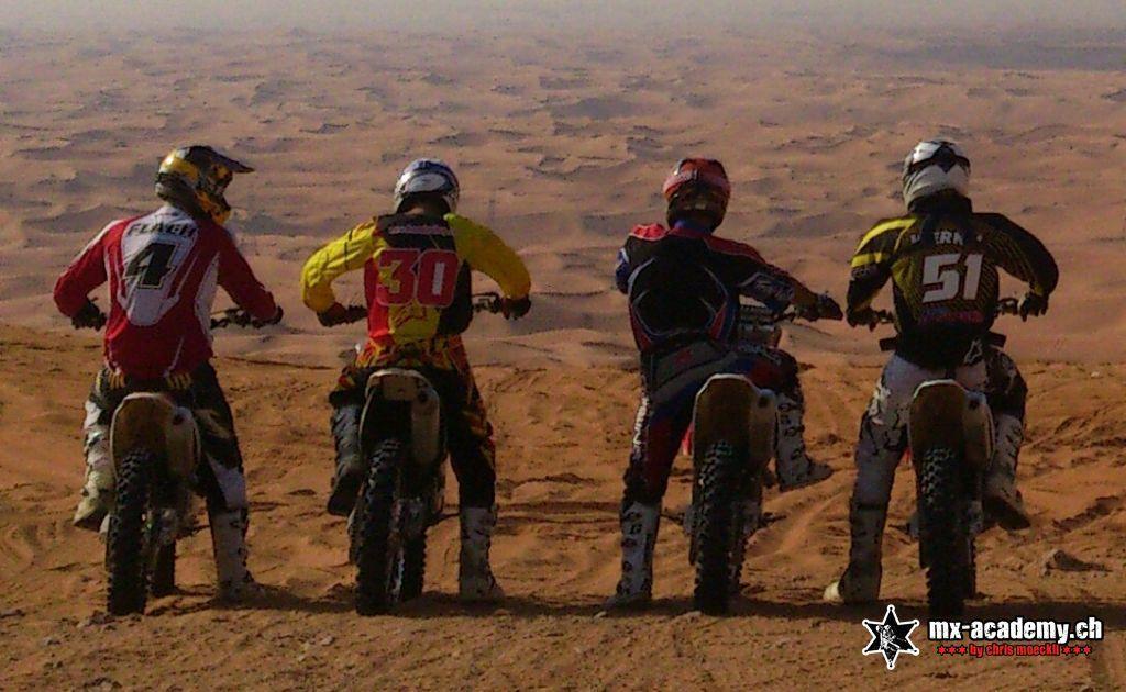 Vier Motocross-Fahrer schauen gemeinsam über die Dünenlandschaft bei Dubai