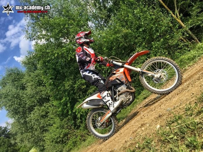 Fahrer mit orangem Motocross Motorrad am steilen Hang im Training